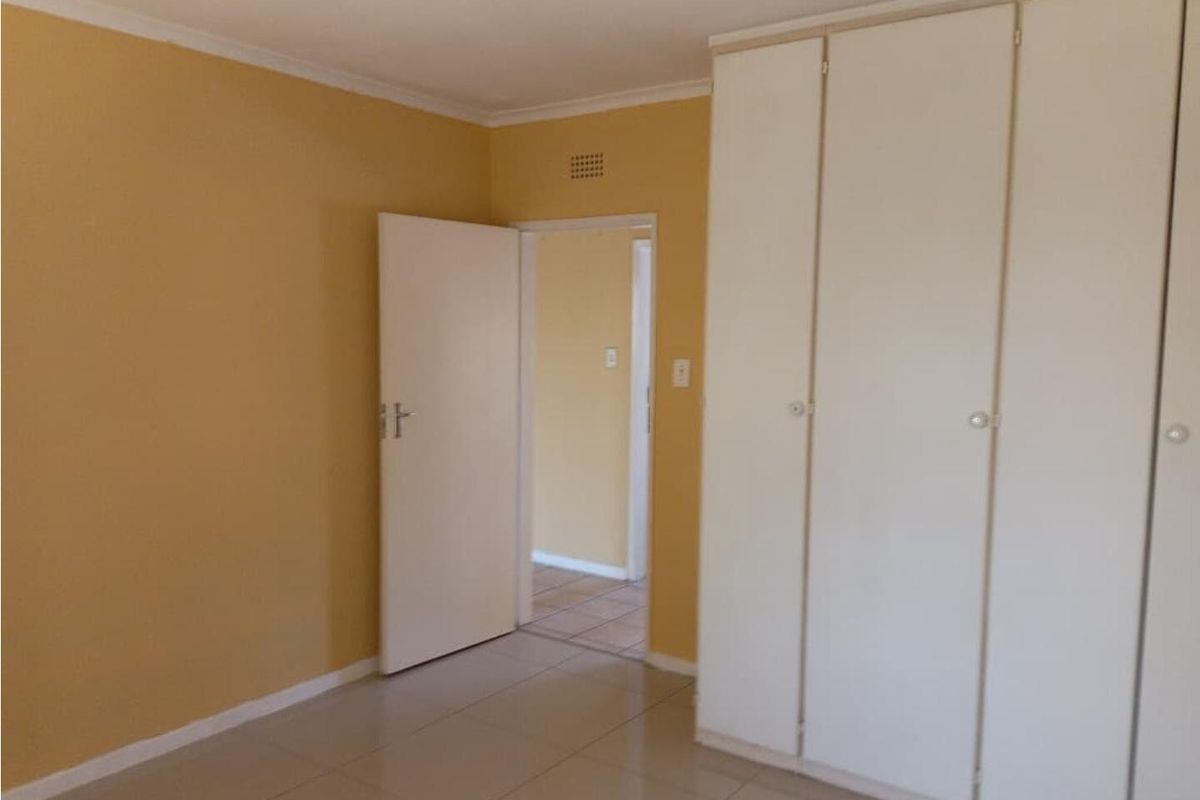 A bedroom featuring built-in cupboards and tiled flooring, with a doorway leading to an adjacent room.