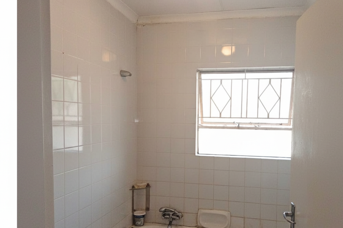 A functional bathroom featuring white wall tiles, a shower-over-bath configuration, and a window with security bars.