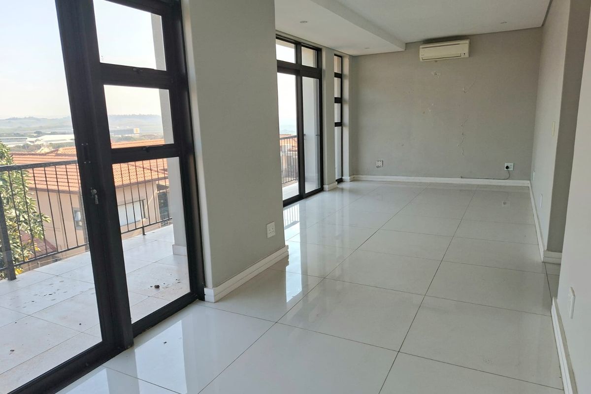 Spacious, light-filled living area featuring large glass sliding doors leading to a balcony, tiled flooring, and a wall-mounted air conditioning unit.