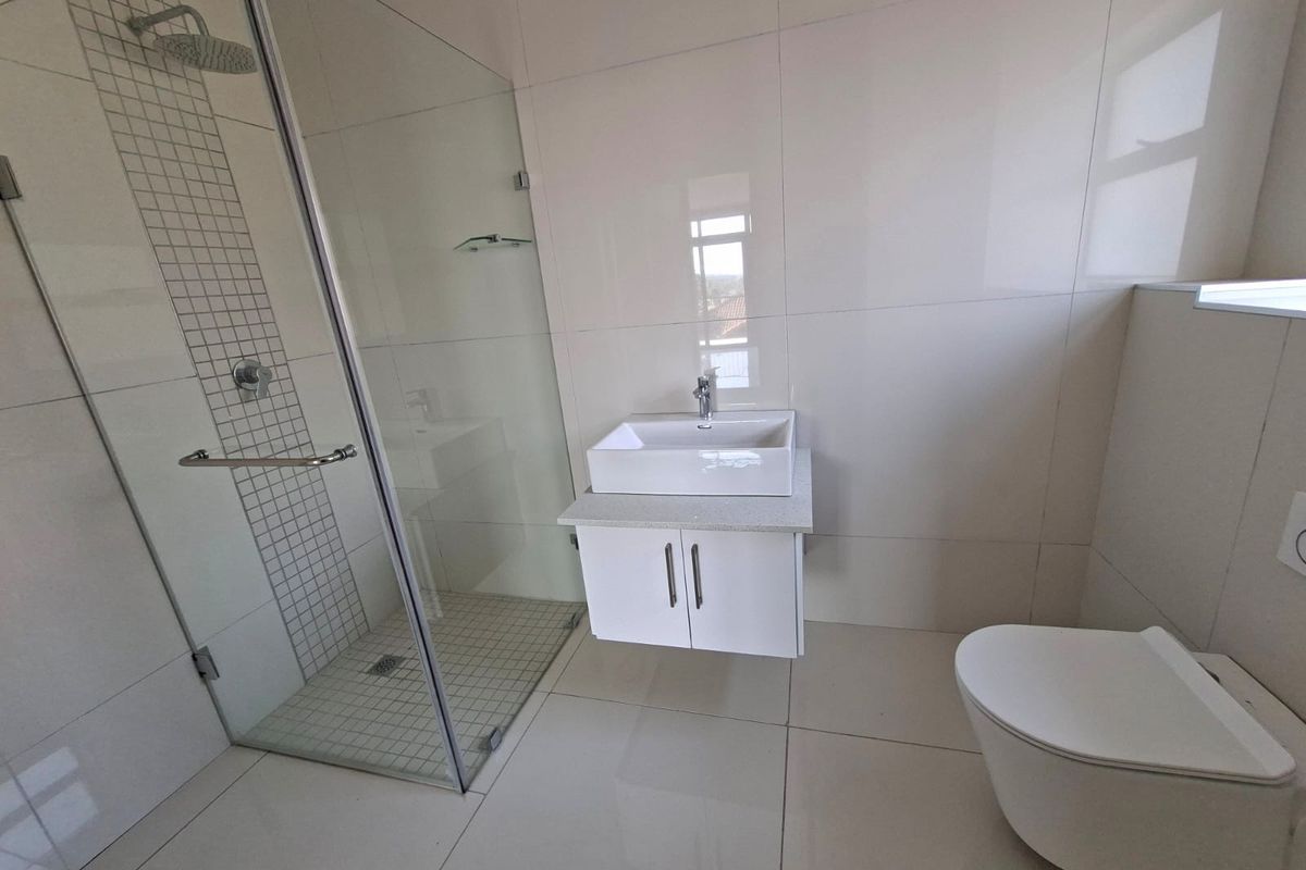 Modern bathroom featuring a frameless glass shower, wall-mounted vanity with a vessel sink, and a contemporary wall-hung toilet with large-format floor and wall tiles.