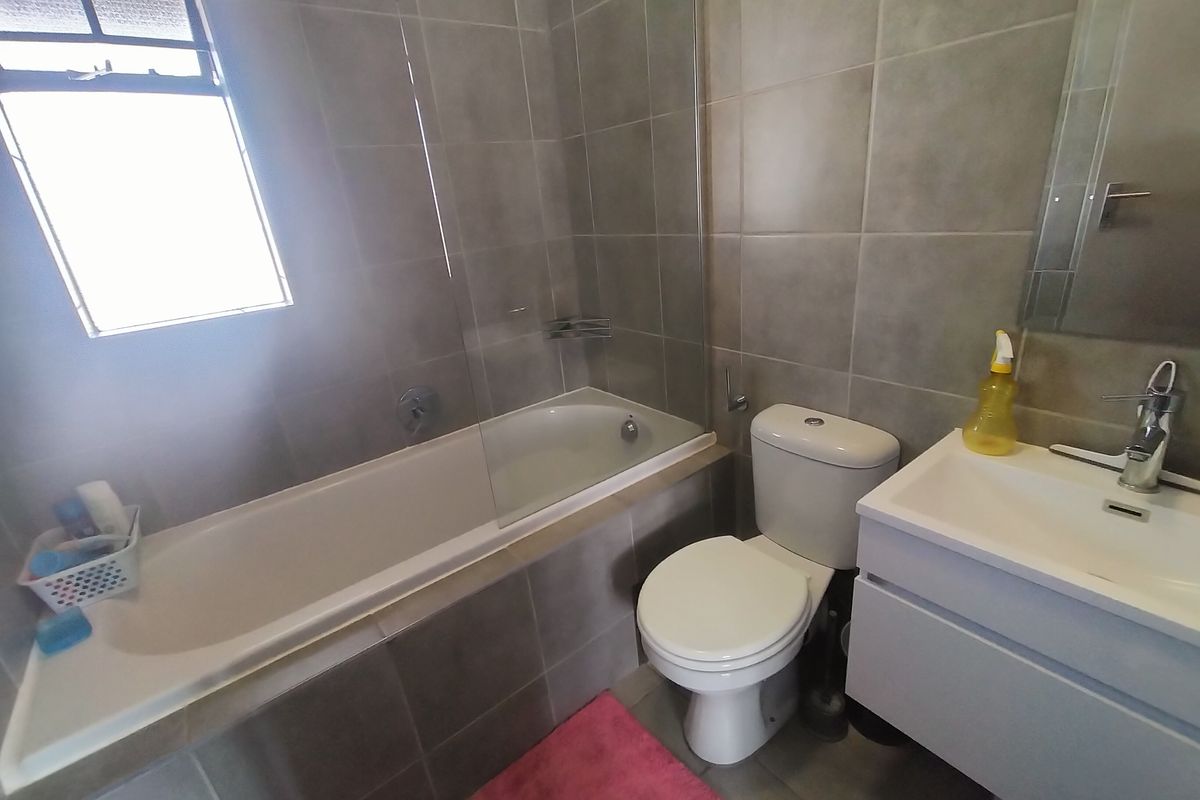 A modern bathroom featuring a built-in bathtub with a glass screen, a wall-mounted vanity with a basin, and neutral floor-to-ceiling wall tiles.