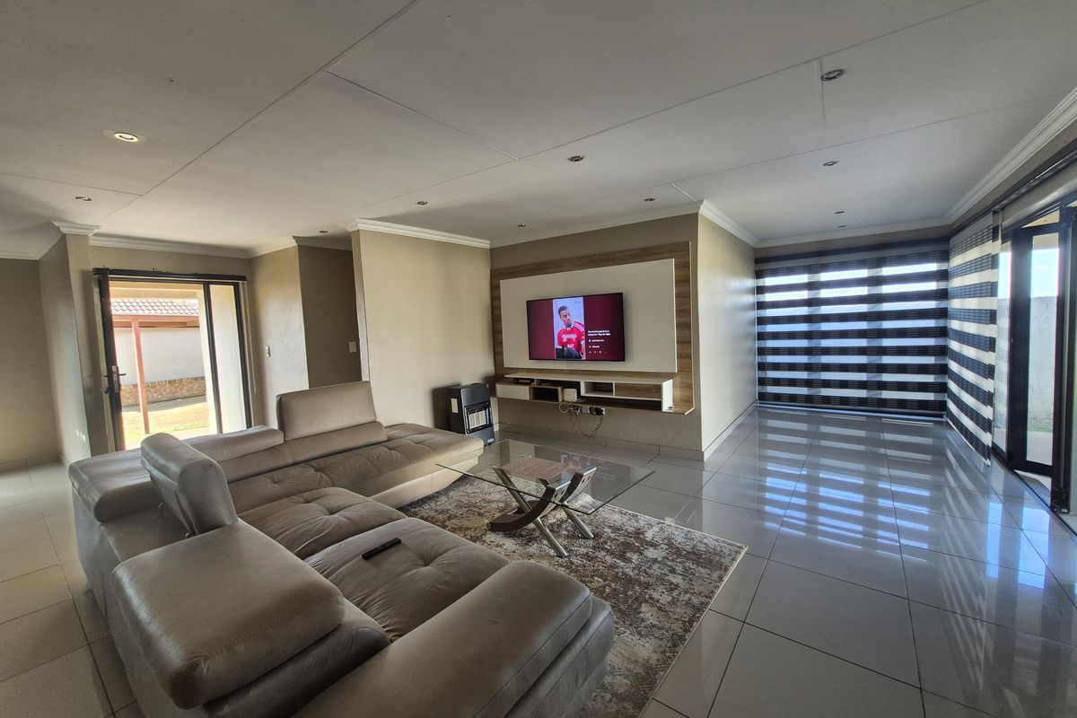 Spacious open-plan living area featuring large format floor tiles, recessed ceiling lighting, and a built-in media wall with integrated shelving.