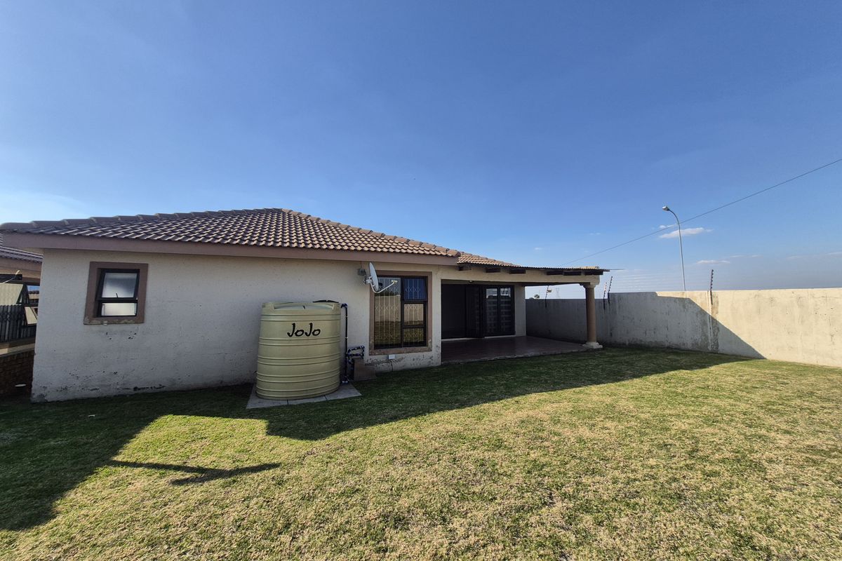 Rear view of the property featuring a covered patio, a water storage tank, and a spacious lawn enclosed by boundary walls.