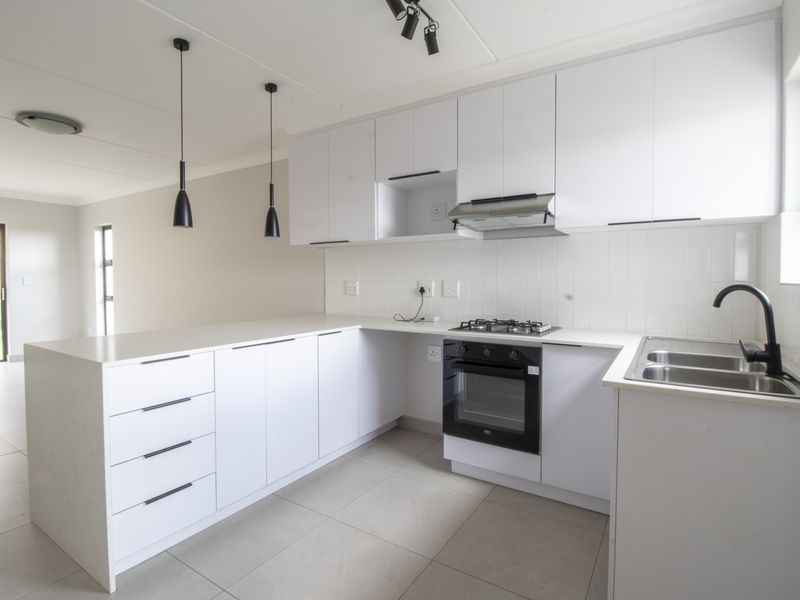 Modern kitchen featuring white cabinetry, stone countertops, gas hob, built-in oven, extractor fan, and double bowl sink with contemporary finishes.