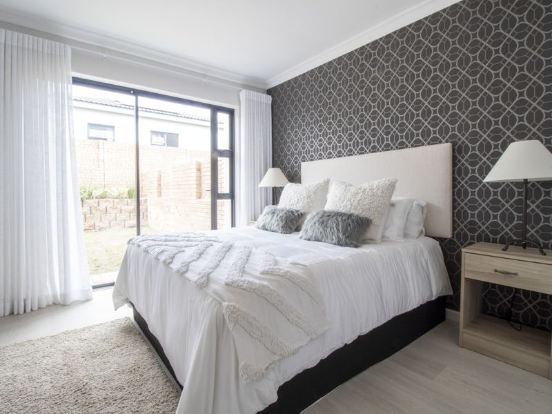 A well-lit bedroom featuring a patterned accent wall, modern flooring, and a large sliding glass door providing direct access to the rear garden area.