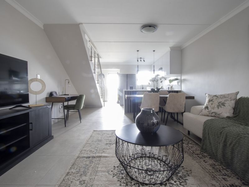 A bright open-plan living and kitchen area featuring tiled floors, a modern staircase, and a functional kitchen island with pendant lighting.