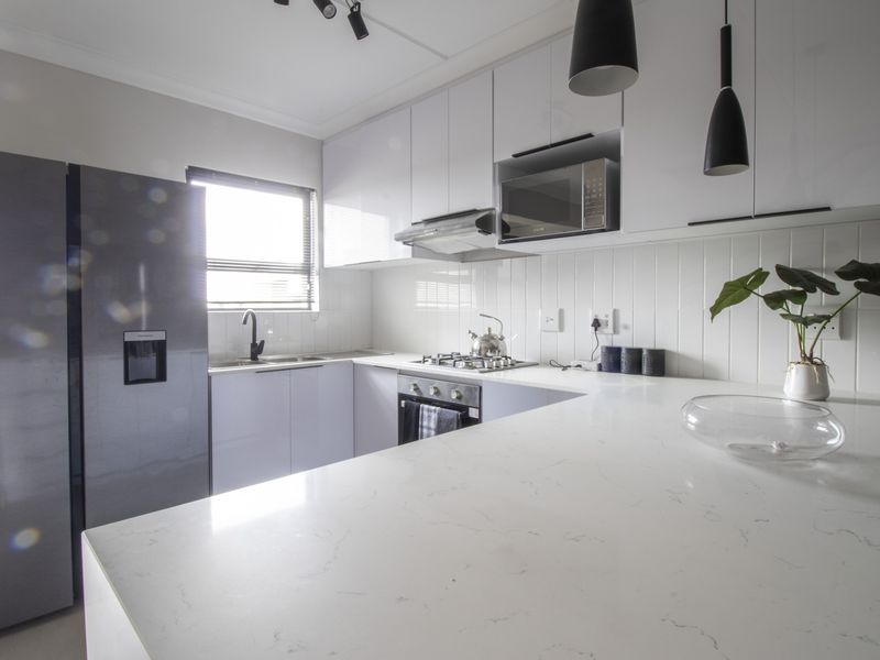 Modern kitchen featuring sleek white cabinetry, quartz countertops, subway tile backsplash, and integrated appliances including a gas hob and built-in oven.