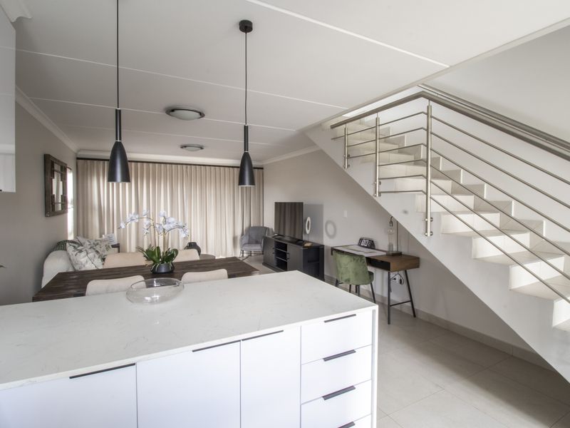 Modern open-plan living area featuring a sleek kitchen island with stone countertops, tiled flooring, and a contemporary staircase with stainless steel balustrades.