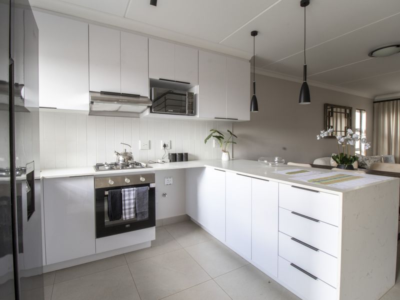 Modern kitchen featuring white cabinetry, stone countertops, built-in oven, gas hob, and integrated microwave, seamlessly flowing into the adjacent living area.