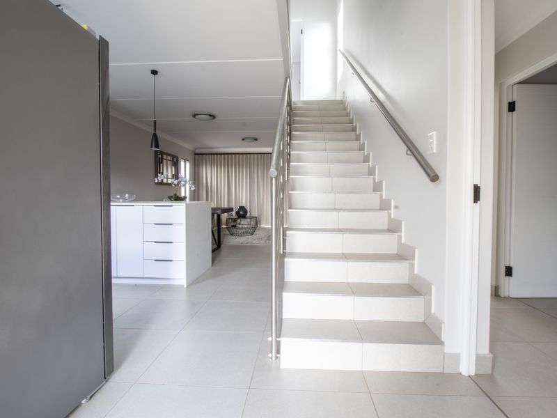 Open plan living area featuring a modern tiled staircase with stainless steel handrail, leading towards a contemporary kitchen island and bright living space.