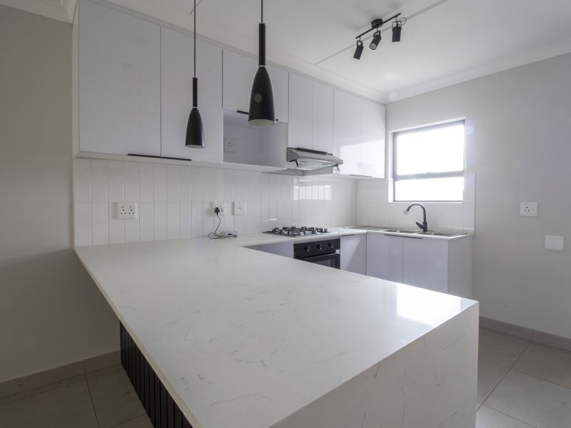 Modern kitchen featuring white cabinetry, stone countertops, gas hob, built-in oven, and sleek black fixtures in a clean, contemporary design.