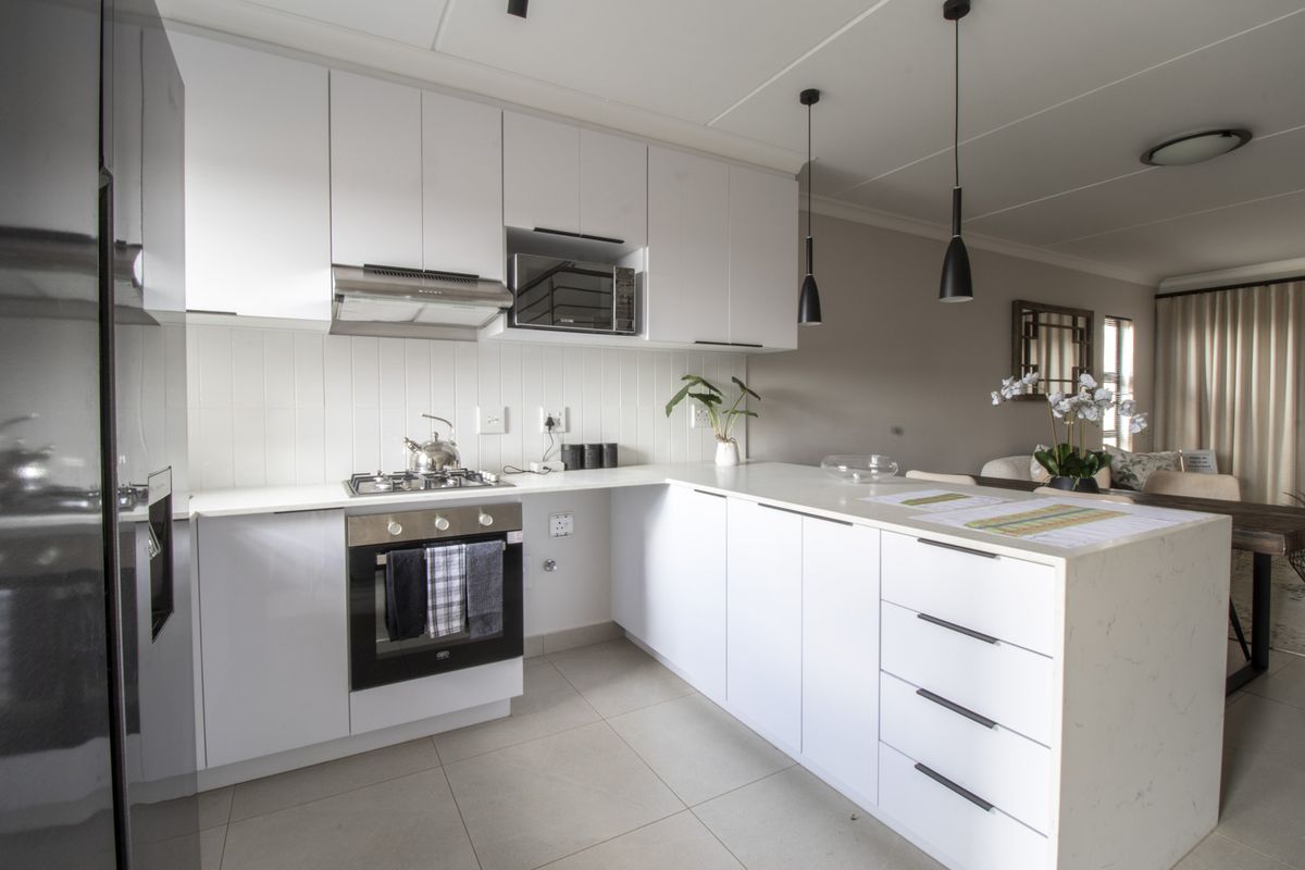 Modern kitchen featuring white cabinetry, stone countertops, built-in oven, gas hob, and integrated microwave, seamlessly flowing into the adjacent living area.