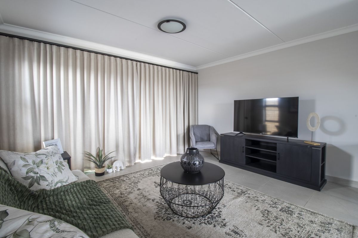 A well-maintained living room featuring neutral tiled flooring, a ceiling light fixture, and full-length curtain tracks.