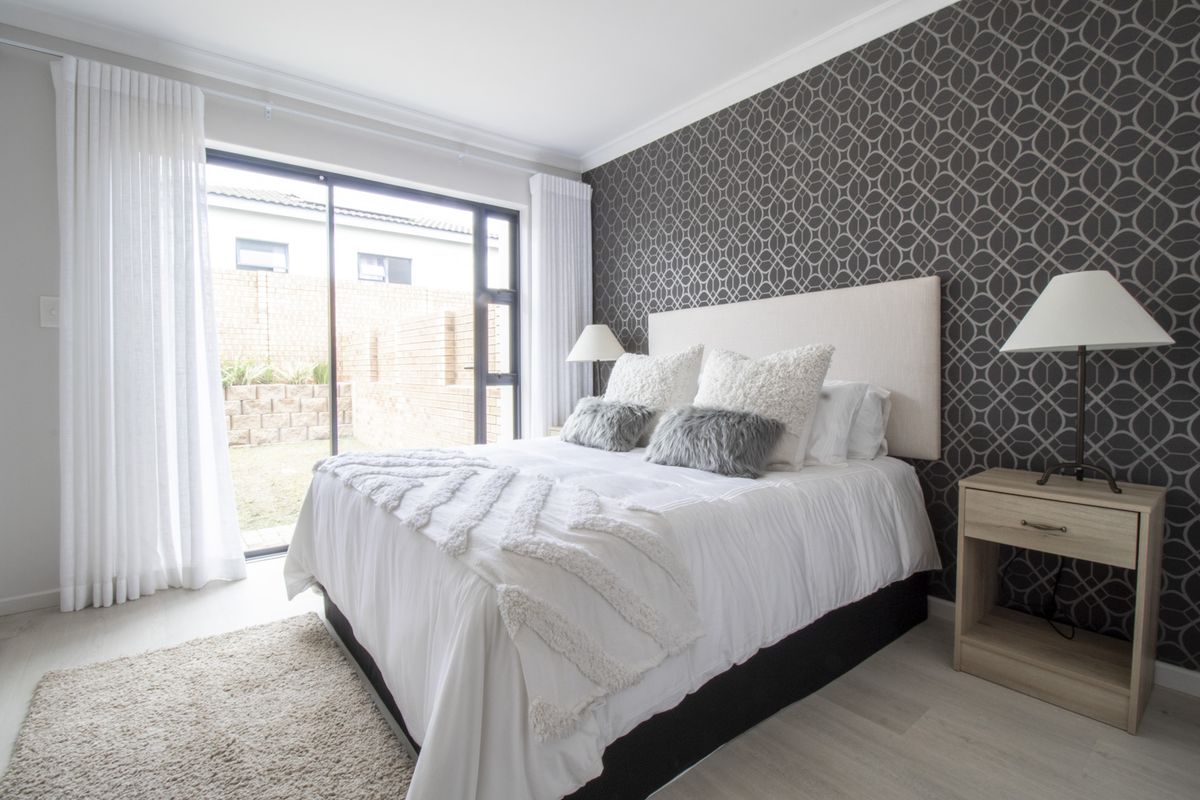 A well-lit bedroom featuring a patterned accent wall, modern flooring, and a large sliding glass door providing direct access to the rear garden area.