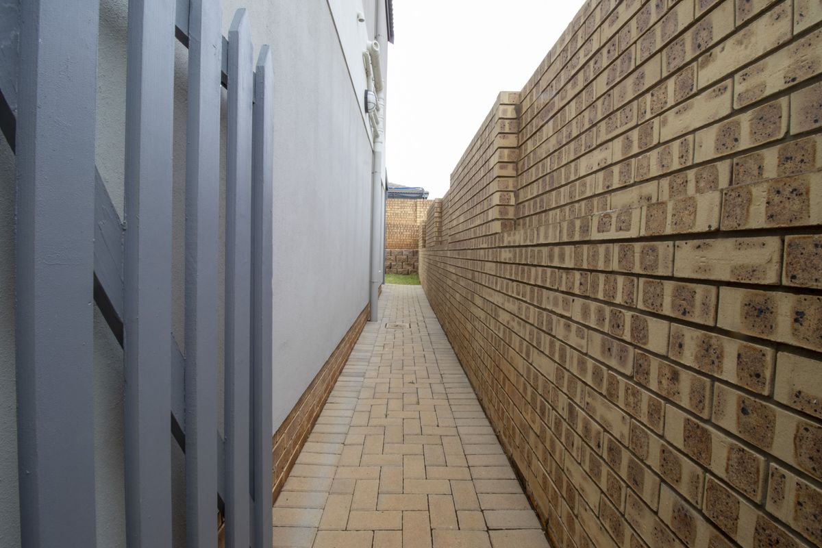 A narrow side passage featuring paved flooring and a sturdy brick boundary wall, providing clean and functional access along the side of the townhouse.