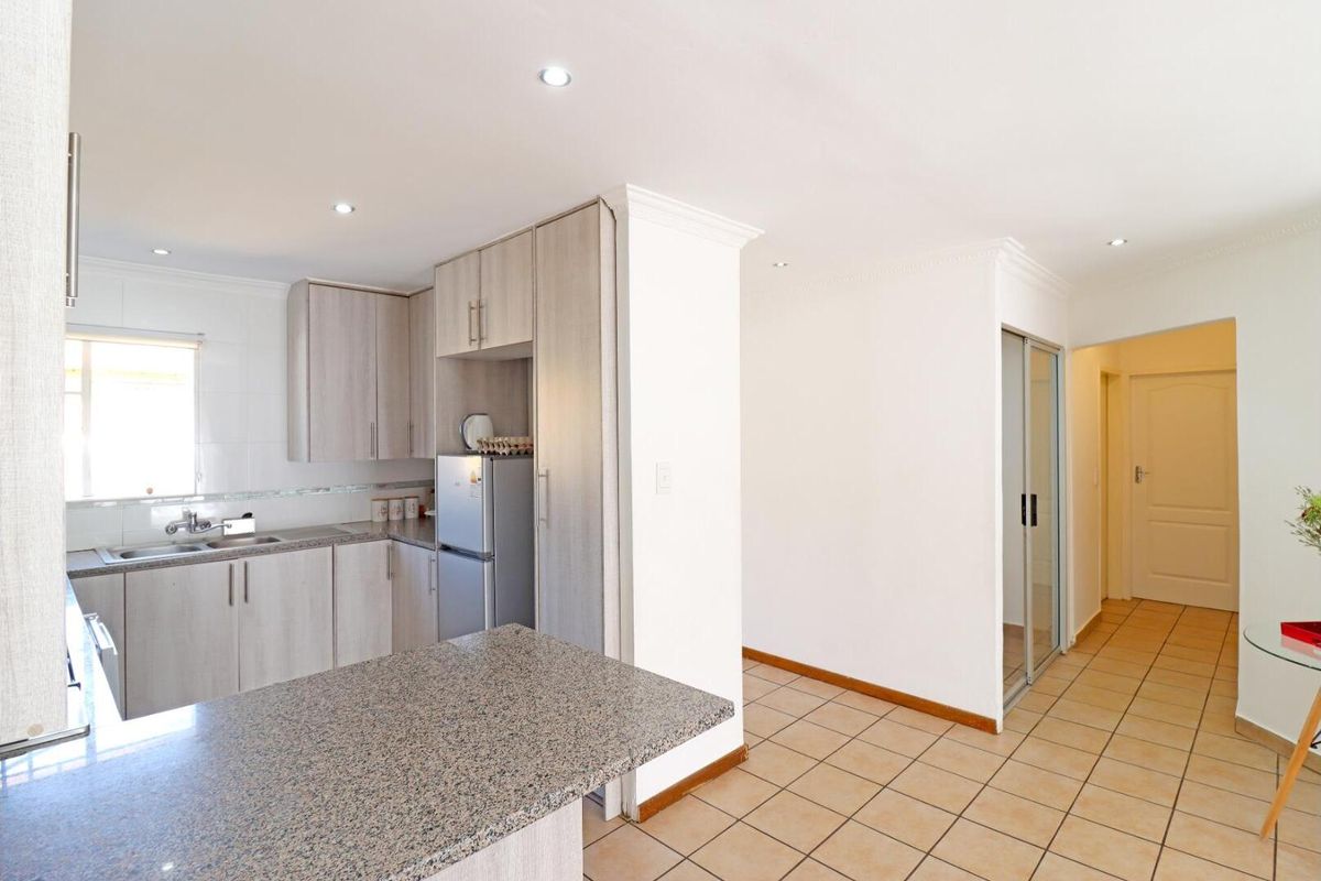 A functional kitchen featuring light wood-grain cabinetry, granite countertops, and a breakfast bar, seamlessly flowing into the tiled hallway and living area.
