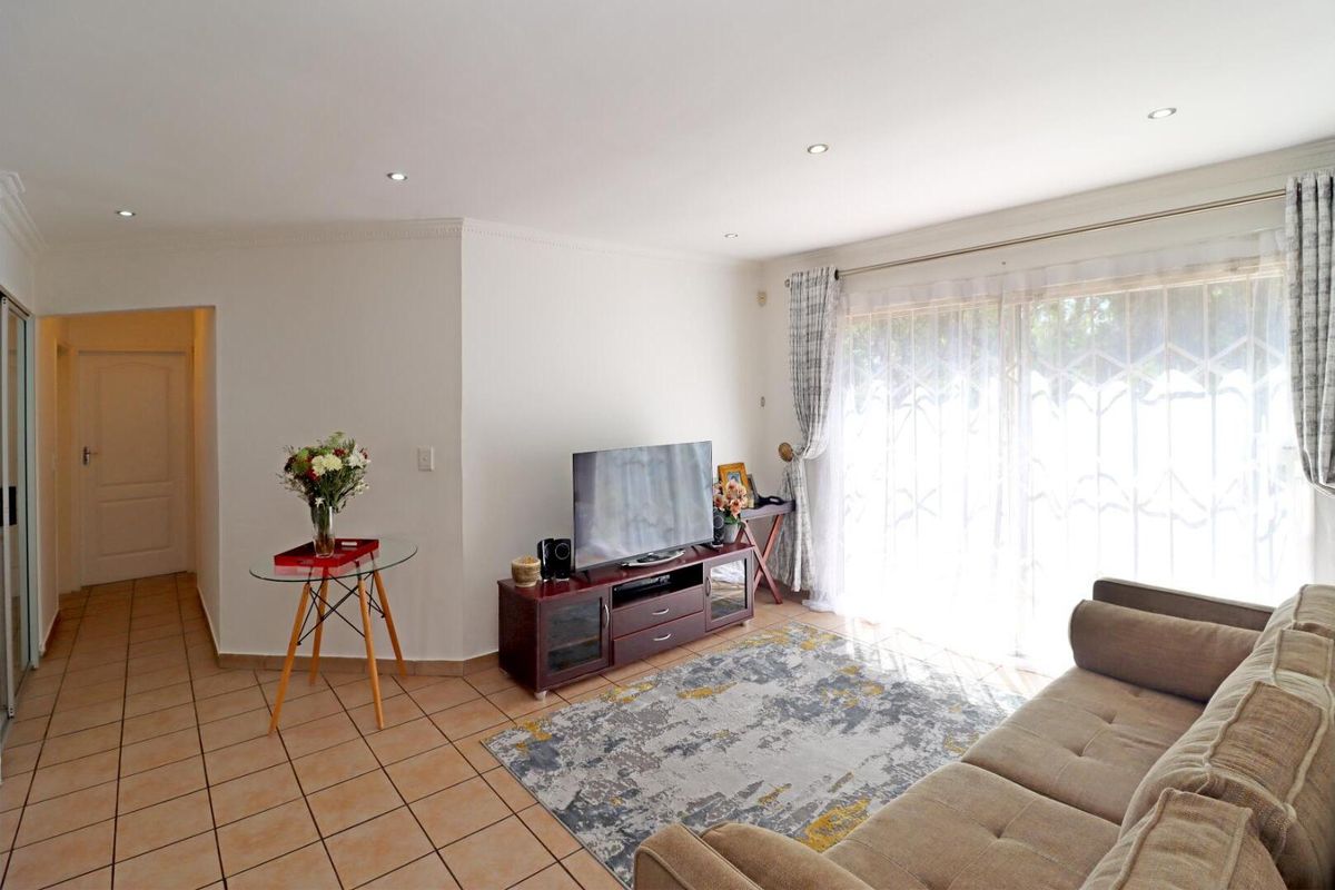 A bright living room featuring tiled flooring, recessed ceiling lighting, and large sliding glass doors with security gates leading to the exterior.