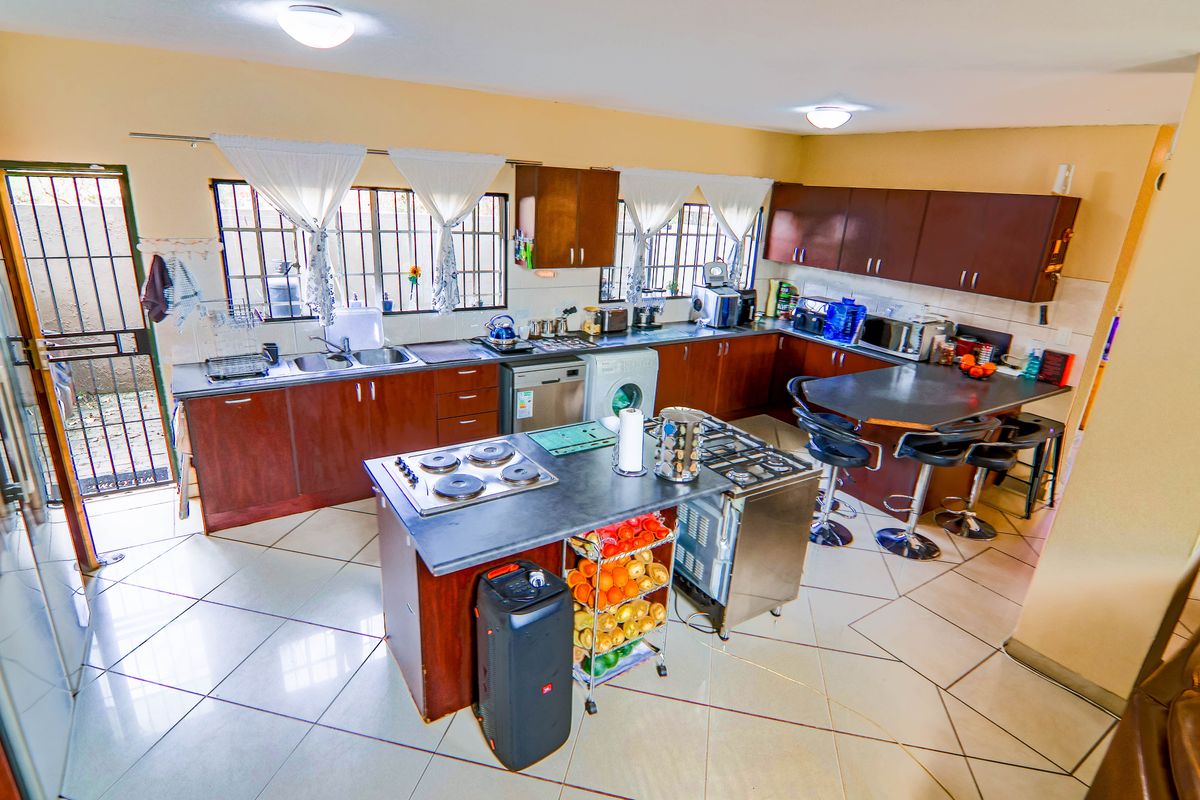 Spacious kitchen featuring dark wood cabinetry, a central island with a built-in hob, tiled flooring, and direct access to an exterior security gate.