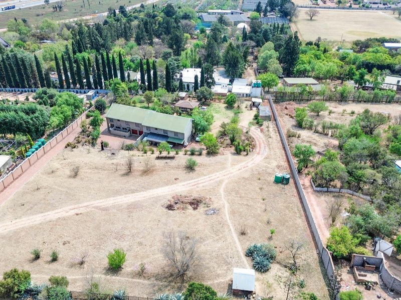 Aerial view of a large residential property featuring a multi-story house, expansive grounds, perimeter fencing, and established trees in a semi-rural setting.