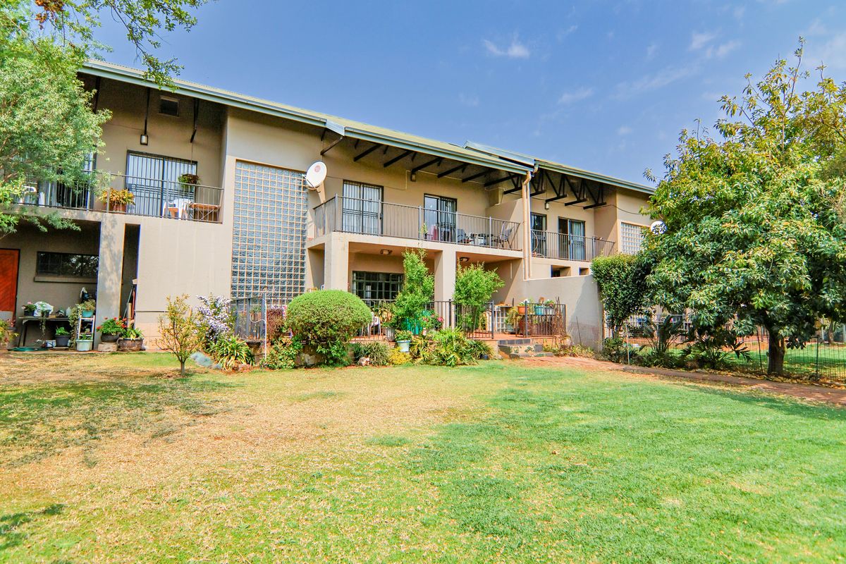 Rear view of a multi-story residential building featuring private balconies, a covered patio area, and a spacious shared garden.