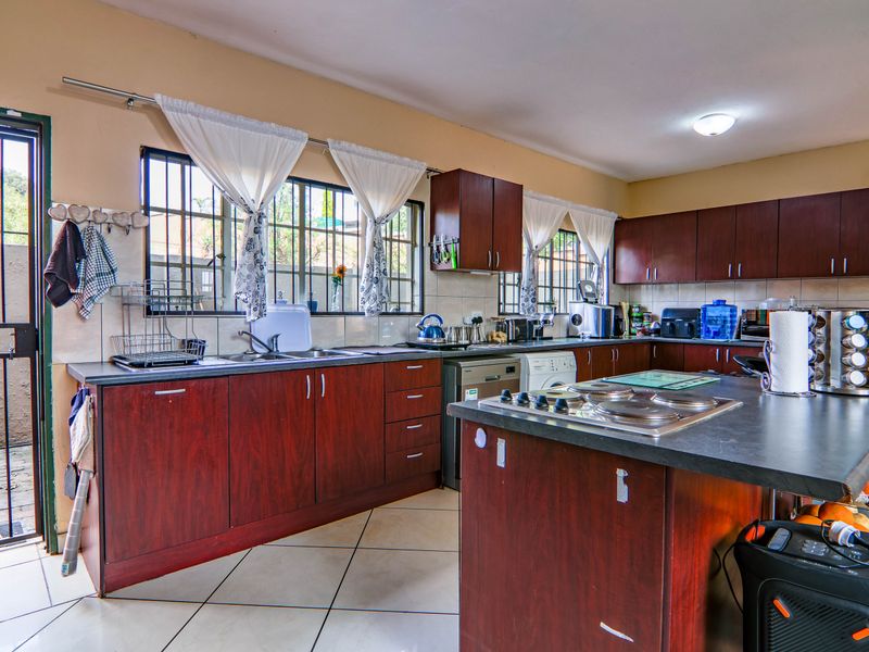A functional kitchen featuring dark wood cabinetry, laminate countertops, a built-in hob, and tiled flooring with direct access to an exterior area.