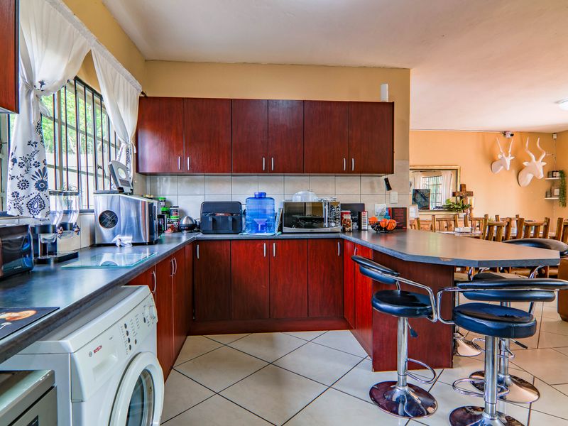 A functional kitchen featuring dark wood cabinetry, laminate countertops, a breakfast bar, and tiled flooring, seamlessly connected to the adjacent living area.