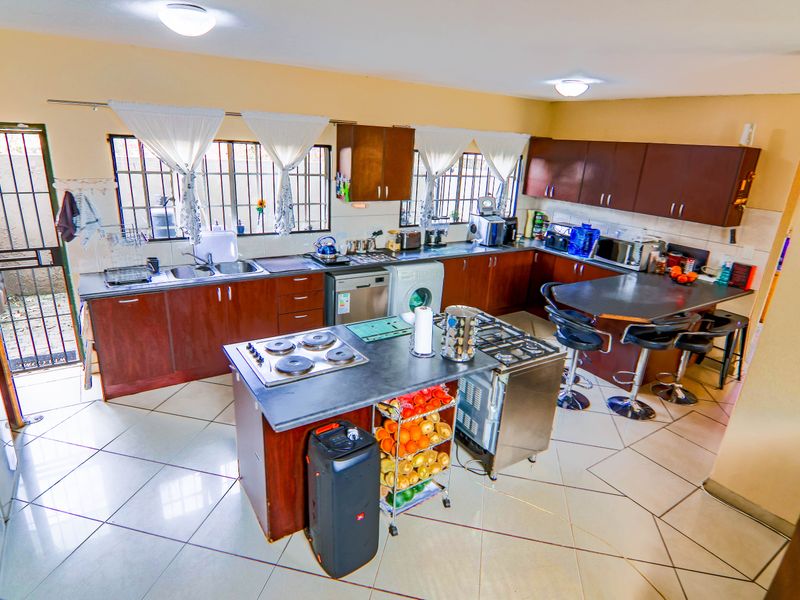 Spacious kitchen featuring dark wood cabinetry, a central island with a built-in hob, tiled flooring, and direct access to an exterior security gate.