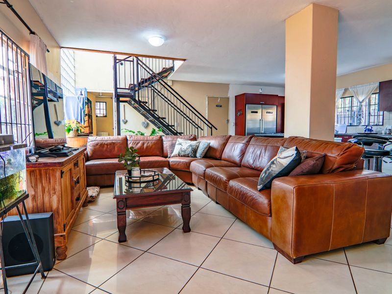 Spacious open-plan living area featuring ceramic tile flooring, a central structural column, and a metal staircase leading to the upper level.