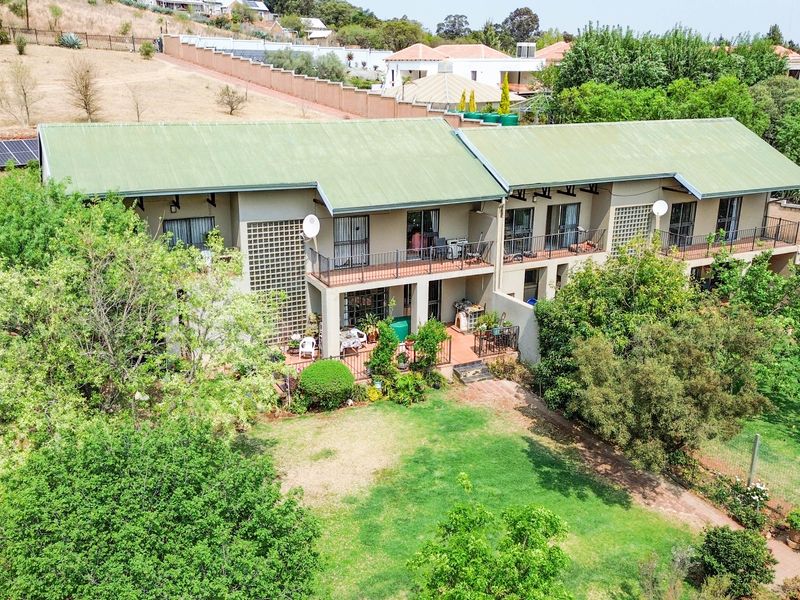 Aerial view of a multi-unit residential property featuring green metal roofing, private balconies, and a spacious landscaped garden area.