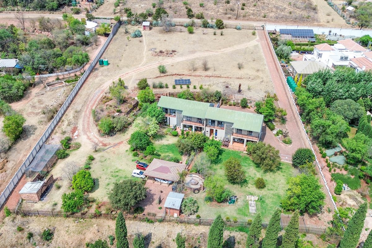 Aerial view of a large residential property featuring a main dwelling, expansive garden, outbuildings, solar panels, and perimeter fencing on a spacious plot.