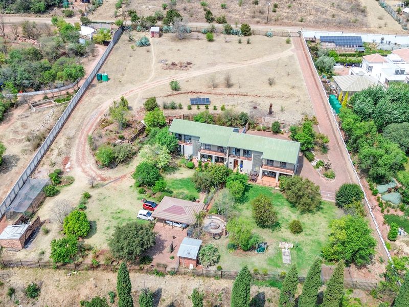 Aerial view of a large residential property featuring a main dwelling, expansive garden, outbuildings, solar panels, and perimeter fencing on a spacious plot.