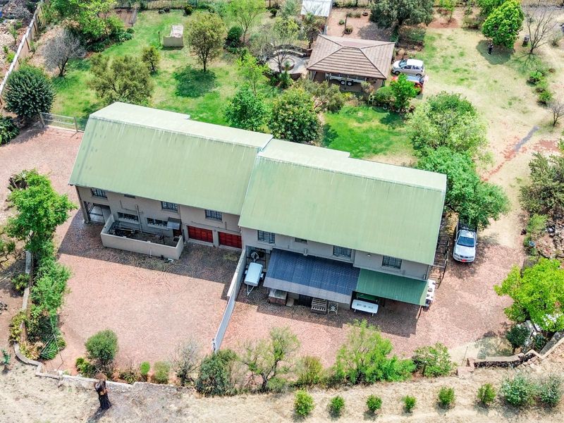 Aerial view of a large residential property featuring a metal-roofed house, expansive garden, paved driveway, and perimeter fencing.