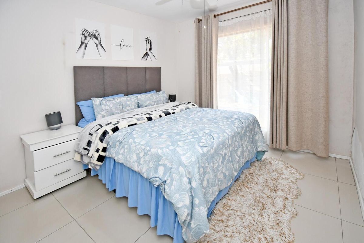 A well-maintained bedroom featuring neutral tiled flooring, a ceiling fan, and a large sliding glass door providing natural light.