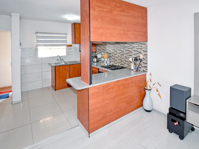 Open plan kitchen featuring wood-look cabinetry, granite countertops, and a mosaic tile backsplash, seamlessly connecting to the living area.