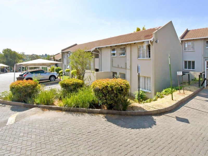 Exterior view of an apartment complex featuring a paved driveway, carport parking, and established garden beds with tiled roofing.
