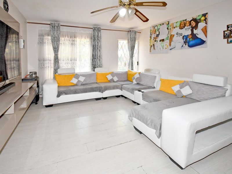 A spacious living room featuring light-toned laminate flooring, a ceiling fan, and a built-in media console, offering a comfortable and functional living space.