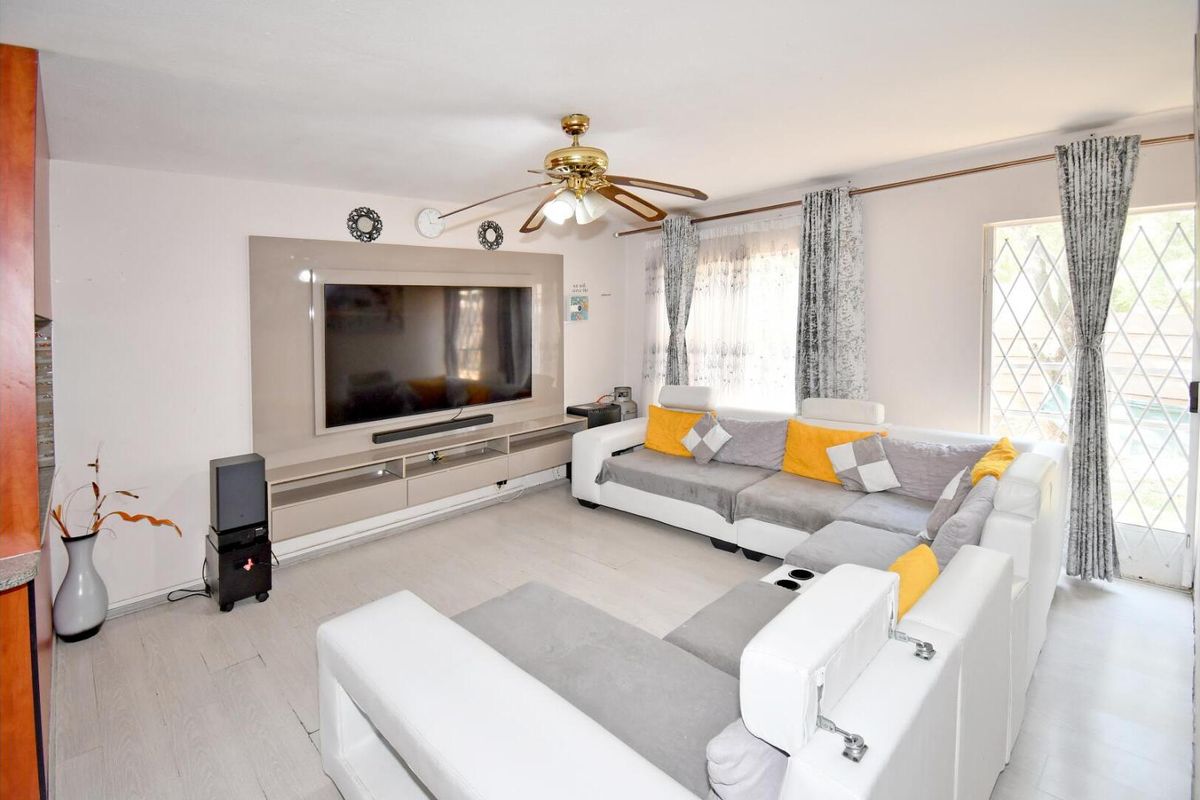 A well-maintained living room featuring a built-in media console, ceiling fan, and direct access to an outdoor area through a security gate.