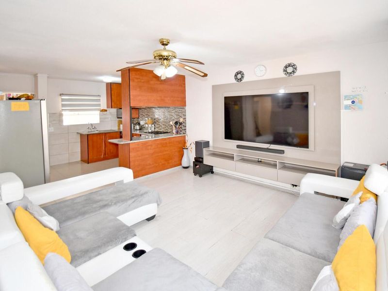 Open-plan living area featuring a modern kitchen with wood-finish cabinetry, stone countertops, and a dedicated media wall, creating a functional and cohesive living space.
