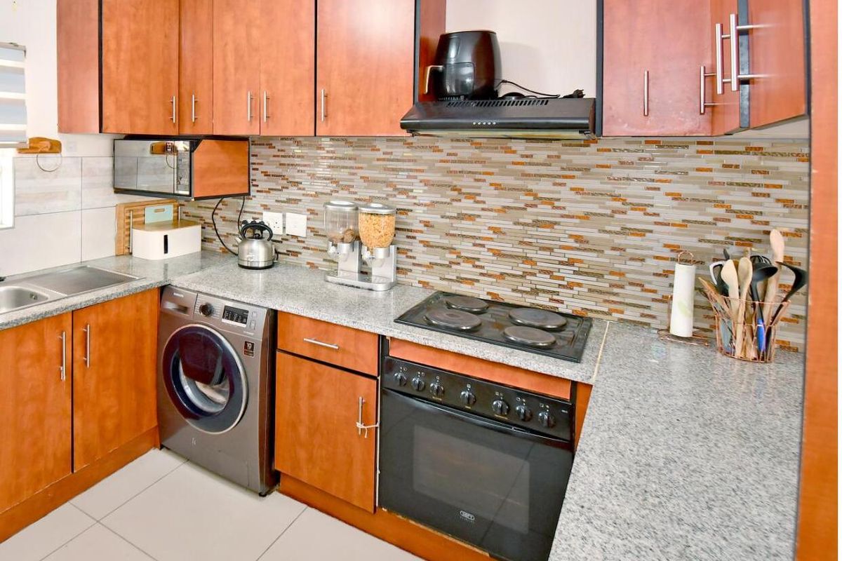 A functional kitchen featuring wood-tone cabinetry, granite countertops, a mosaic tile backsplash, and integrated appliances including an oven and hob.
