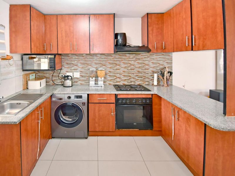 A functional U-shaped kitchen featuring wood-finish cabinetry, granite countertops, a mosaic tile backsplash, and integrated appliances including an oven and hob.