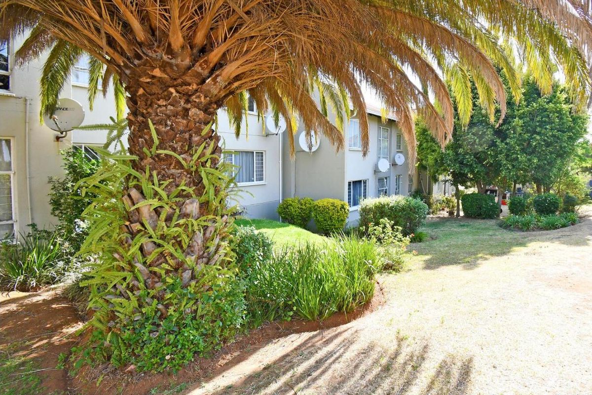 A view of the apartment building's rear exterior, featuring a landscaped garden area with mature trees and lawn.