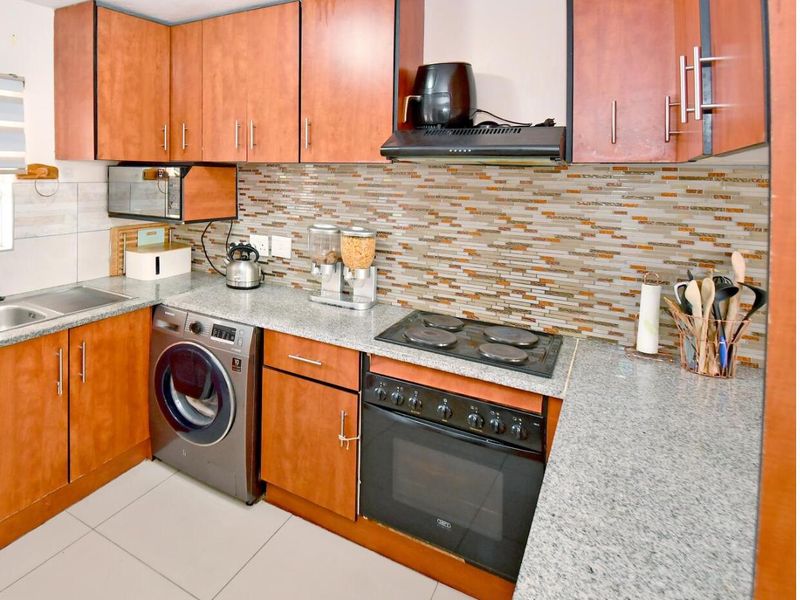 A functional kitchen featuring wood-tone cabinetry, granite countertops, a mosaic tile backsplash, and integrated appliances including an oven and hob.