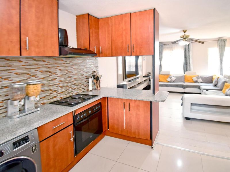 Open-plan kitchen featuring wood-finish cabinetry, granite countertops, and a mosaic backsplash, seamlessly flowing into the adjacent living area.