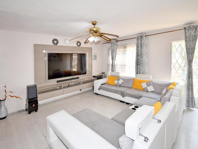 A well-maintained living room featuring a built-in media console, ceiling fan, and direct access to an outdoor area through a security gate.