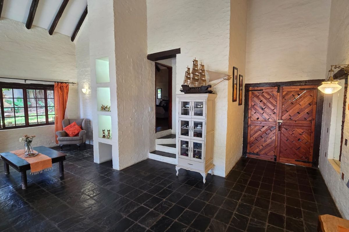 Spacious living area featuring high vaulted ceilings with exposed timber beams, textured white walls, and dark slate tile flooring with double timber entrance doors.