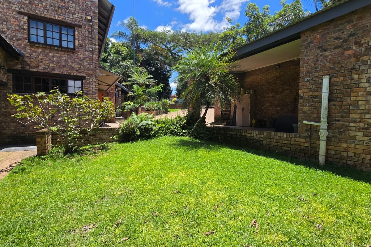 A rear garden area featuring a lawn, paved walkway, and face brick exterior walls with a covered patio space.