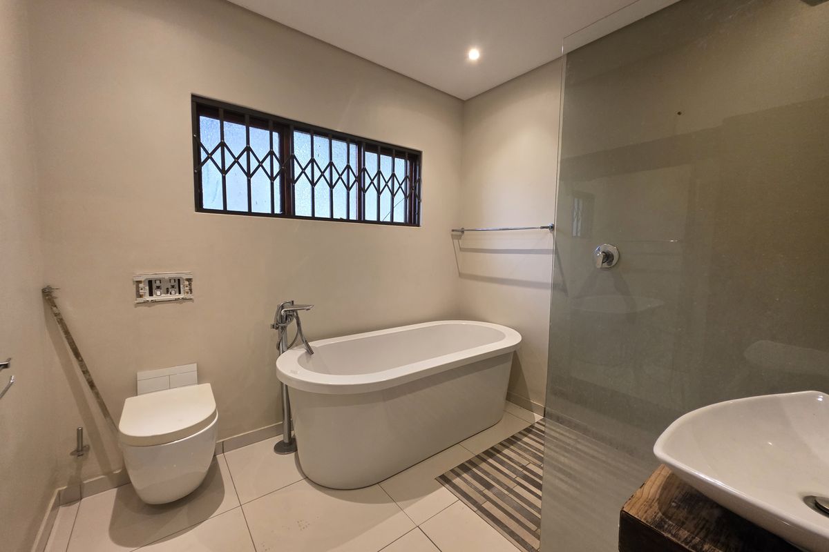 Modern bathroom featuring a sleek freestanding bathtub, wall-hung toilet, glass-enclosed shower, and a contemporary vessel sink on a rustic vanity.
