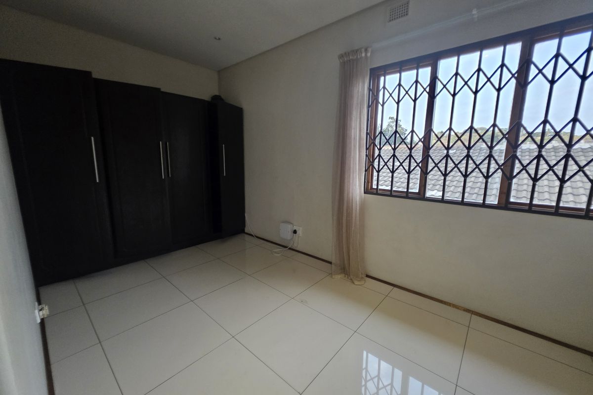 A clean, empty bedroom featuring neutral tiled flooring, built-in dark cabinetry, and a window fitted with a security gate.