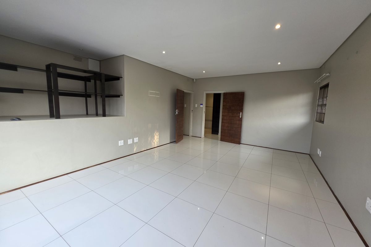 A spacious, empty living area featuring neutral wall tones, polished porcelain floor tiles, recessed downlights, and a built-in shelving unit.