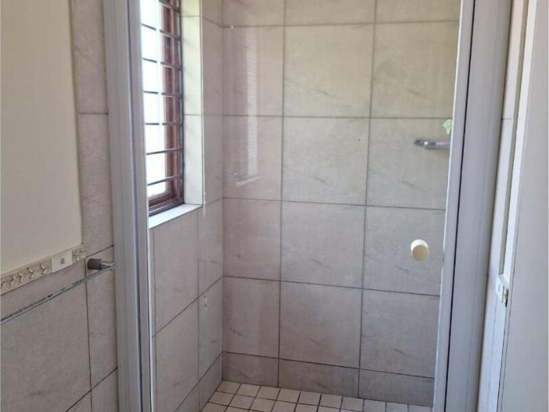 A functional bathroom shower enclosure featuring tiled walls, a tiled floor, and a window with security bars.